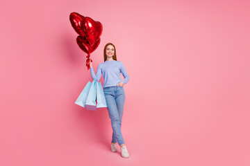 Full size photo of satisfied girl wear blue pullover hold red balloons get presents in shopping bags isolated on pink color background