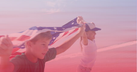 Caucasian brother and sister with american flags running at the beach