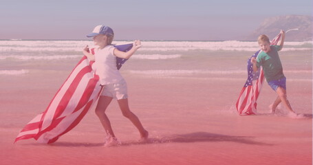Image of smiling caucasian siblings with american flags running at beach
