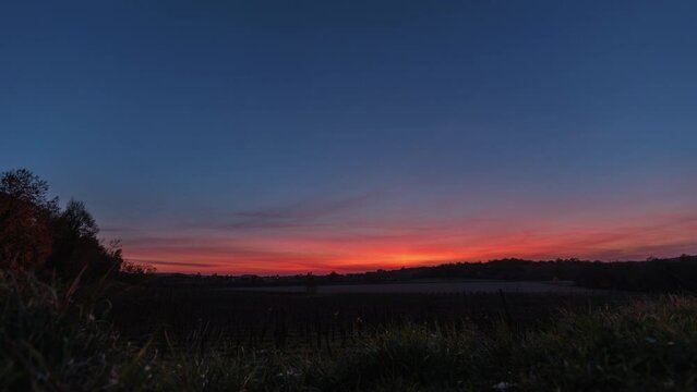 breve timelapse video, con visuale panoramica, che mostra un ambiente di campagna, durante un bellissimo e colorato tramonto, con il sole che cala oltre l'orizzonte, in un cielo sereno