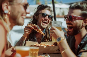 Foto op Plexiglas Happy friends in sunglasses eating pizza and drinking beer at a rooftop party, laughing while sitting at a table with a box of pizzeria food © Kien