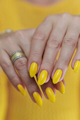 Female hand with long nails and a bottle of bright yellow orange nail polish	