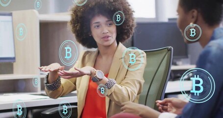 Image of bitcoin symbols over diverse colleagues discussing work in office