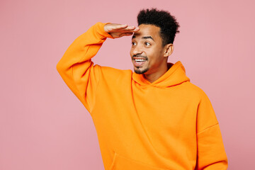 Young man of African American ethnicity wear yellow hoody casual clothes hold hand at forehead look far away distance isolated on plain pastel light pink background studio portrait. Lifestyle concept.