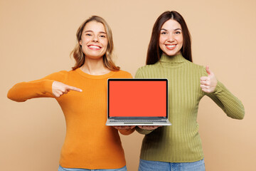 Young friends two IT women wear orange green shirt casual clothes together hold use work on laptop...