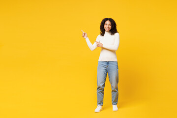 Full body little kid teen girl of African American ethnicity wear white casual clothes point index finger aside on area mock up isolated on plain yellow background studio. Childhood lifestyle concept.