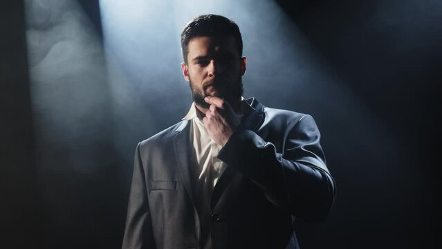 Attractive businessman posing stylishly against a dark background in foggy smoke. Style and confidence concept.