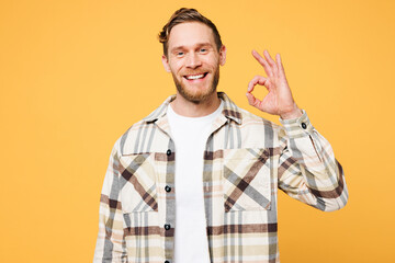 Young smiling happy satisfied cheerful Caucasian man wear brown shirt casual clothes showing okay ok gesture look camera isolated on plain yellow orange background studio portrait. Lifestyle concept.