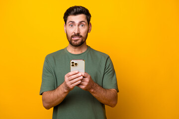 Photo portrait of nice young male hold gadget bite lips nervous wear trendy khaki garment isolated on yellow color background