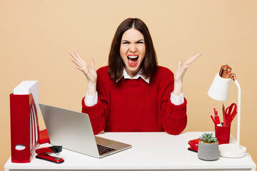 Young sad mad angry employee business woman wear red sweater shirt sit work at office desk with pc...