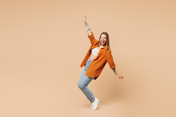 Fototapeta na wymiar Full body young woman she wear orange shirt casual clothes stand on toes leaning back with outstretched hands dance isolated on plain pastel light beige background studio portrait. Lifestyle concept.