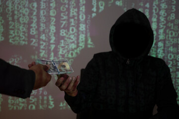 A man wearing a hooded shirt uses a laptop in the dark to hack data in exchange for money.