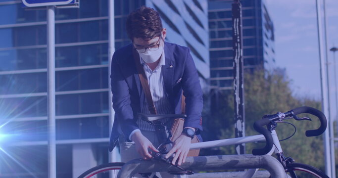 Image of light spots over asian man with face mask locking bicycle - Powered by Adobe