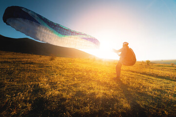 paraglider with a blue parachute takes off. A male athlete stands on the field and lifts a...