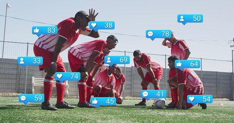 Image of social media icons over tired diverse male soccer players taking break on sports field