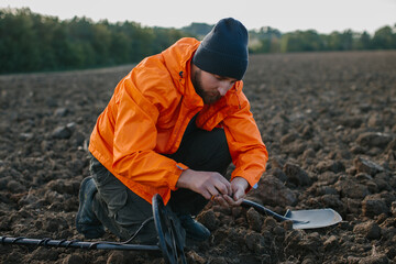 A young man is a treasure hunter. A man holds an ancient coin found with a metal detector.