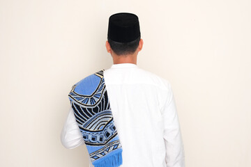 Back view of Moslem man standing with prayer mat on his shoulder