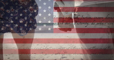 Fototapeta premium Image of American flag waving and constitution text over biracial couple by seaside on summer holida