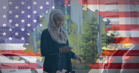 Image of American flag waving with jigsaw puzzles revealing biracial woman in hijab using smartphone - Powered by Adobe