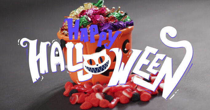 Naklejki Image of happy halloween text over orange pumpkin bucket with sweets
