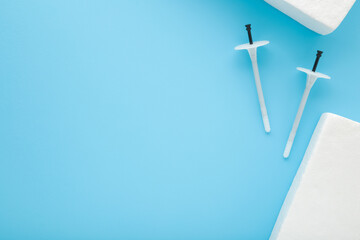 White insulation anchor dowels and styrofoam panels on blue table background. Closeup. Material for house thermal protection. Home facade repair work preparation. Empty place for text. Top down view.