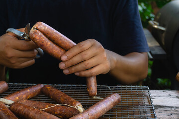A man is cutting a sausage link that uses collagen casing, it will be cooked using the smoking technique
