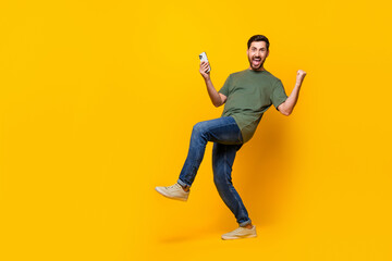 Fototapeta na wymiar Full size photo of attractive young man hold gadget winning raise fists wear trendy khaki clothes isolated on yellow color background