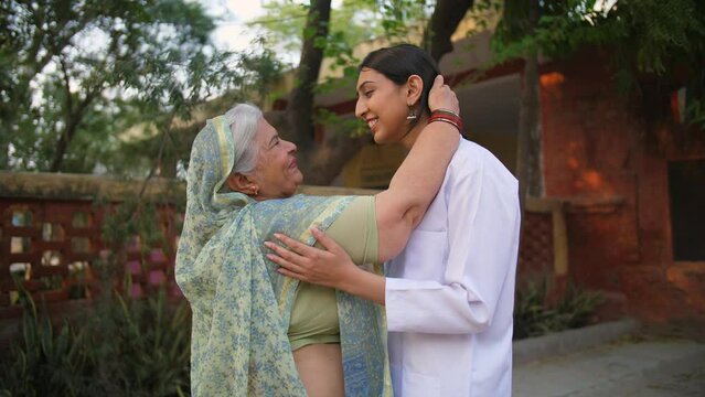 Grey-haired Indian mother giving blessings to her daughter for becoming a doctor - rural lifestyle  proud mother. Old age mother feeling overwhelmed with her daughter's achievements - studious chil...
