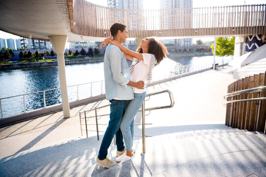 Full body length photo of young family couple spend free time outdoors hugging looking each other bonding laughing at city river pond