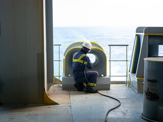 Able seaman crew member of cargo vessel is chipping rust from the ship bollard construction by air...