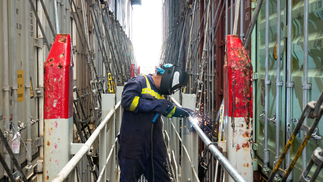 Seaman crew member fitter welder of cargo vessel is repairing ship structure lashing bridge by welding of new pipes dressed with proper ppe