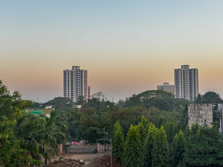 A city skyline with two tall buildings and a forest in the background