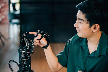 Happy Asian teen boy learns technology by testing a robot hand and arm fostering educational skills...