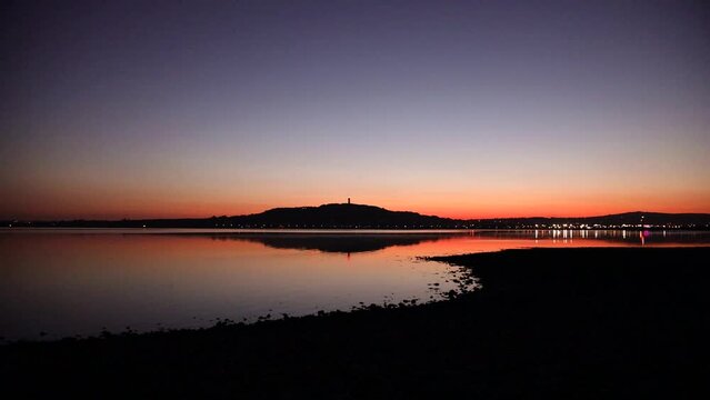 Sunset over Strangford Lough with Scrabo Hill visible. Twinkling lights of Newtownards town. Calm, incoming tide on a summer's evening. Panning shot Northern Ireland