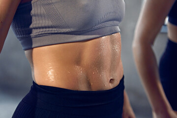 Close up of young woman with athletic body in sportswear wet after productive weightlifting...