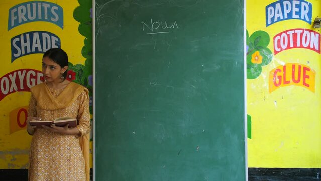 Young age Indian teacher taking english class in village school - government school  teaching noun  blackboard teaching. Desi female teacher introducing noun to her students in class - village life...