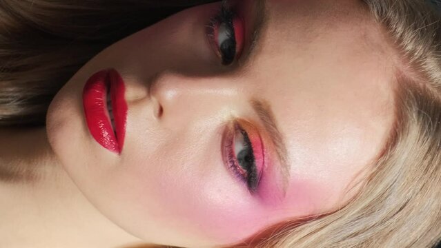 Beautiful model with bright makeup and red lips. Portrait of a girl close-up on a blue background. Vertical video.
