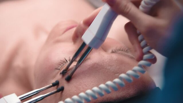 Close-up portrait of a beautiful woman with closed eyes and a skin rejuvenation machine. Salon procedures. Microcurrent therapy