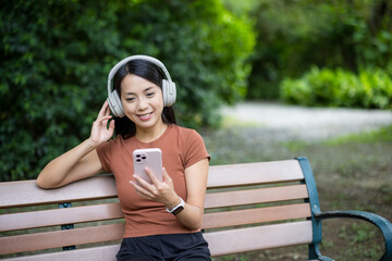 Woman with headphone and look at the mobile phone in park - 758111860