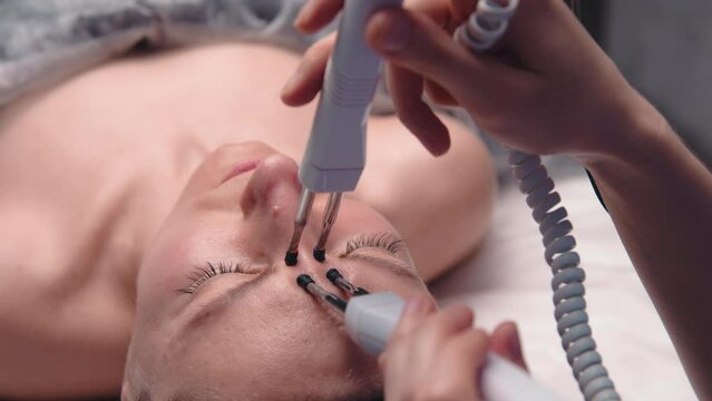 Close-up portrait of a beautiful woman with closed eyes and a skin rejuvenation machine. Salon procedures. Microcurrent therapy