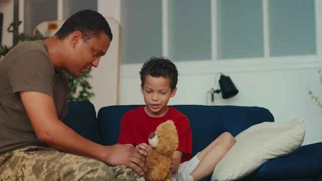 An African American dad in the military playing with son and teddy bear at home