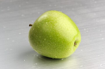Green Apple with Water Drops on Brushed Aluminum Background
