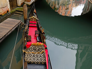 An empty gondola is parked in a Venetian canal. View of the bridge over the canal, reflection of the bridge in the water. Typical narrow street with historical houses in Venice.