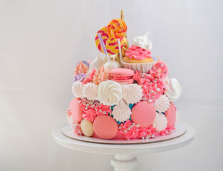 Bright beautiful pink cake with golden fondant horn, twisted lollipops, macaroons and meringues on...