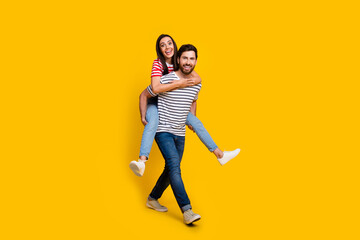 Full length photo of positive couple boyfriend holding on back cute girl walking to empty space isolated on vivid yellow color background
