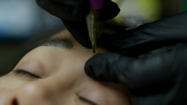 Close up microblading eyebrow tattoo. Beautician in gloves makes permanent makeup correction of the shape of the eyebrows to a young women. Eyebrow tattoo in a beauty salon.