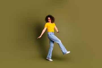 Fototapeta na wymiar Full length body photo of excited girl in yellow t shirt and jeans stylish sunglasses dance boogie woogie isolated on khaki color background