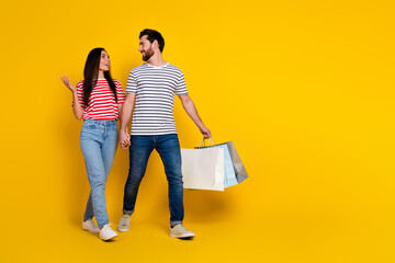 Full length photo of adorable couple wear striped t-shirt jeans walking with new outfit to empty...