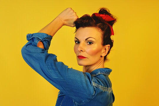 Woman with retro hairstyle raising her hand in fist in front of yellow studio background
