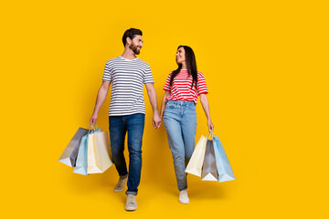 Full length photo of attractive lovely couple wear striped t-shirt hold hands go with shopping bags...